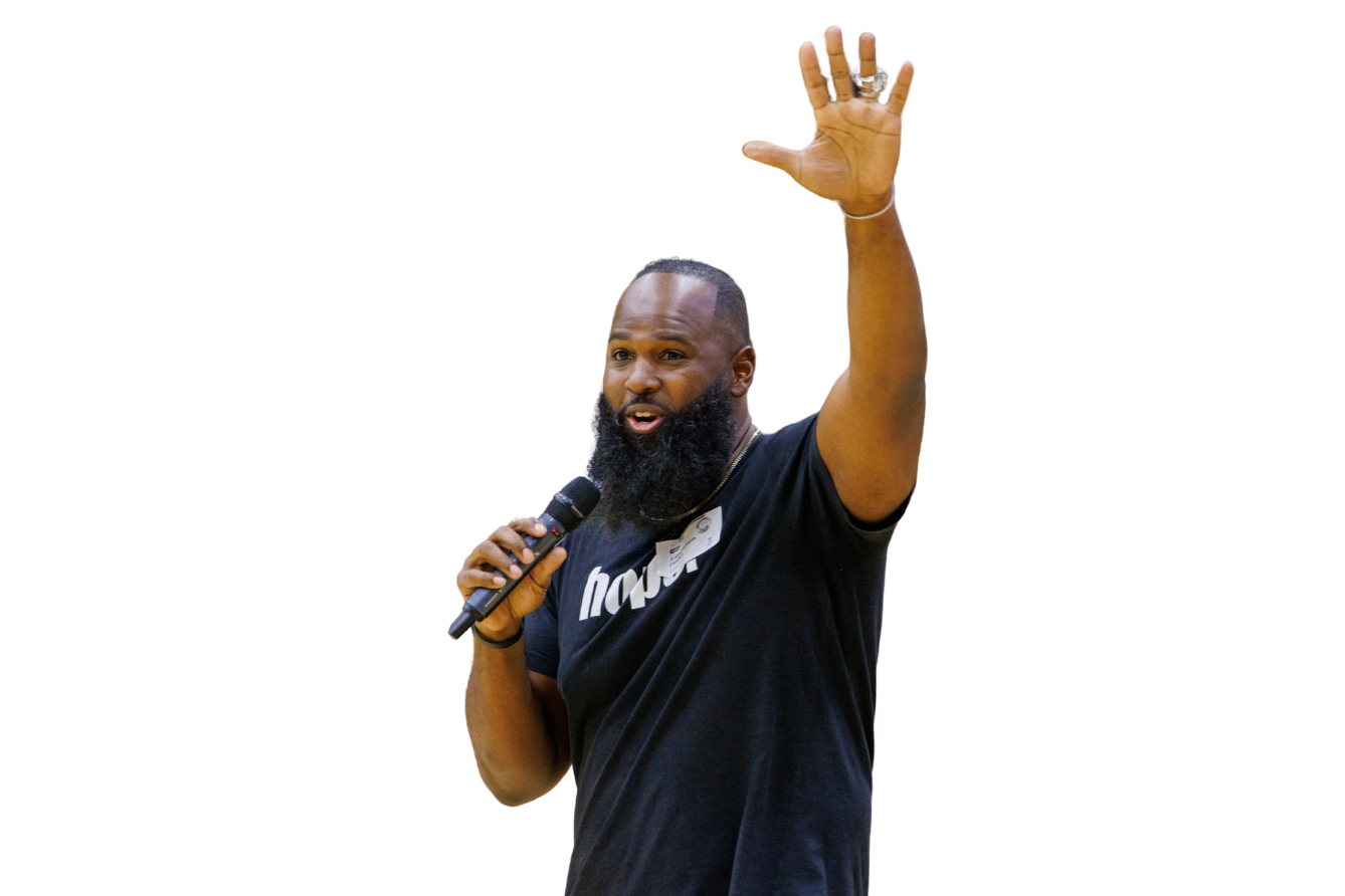 Andre Fluellen speaking to students with a microphone in one hand and the other hand raised high